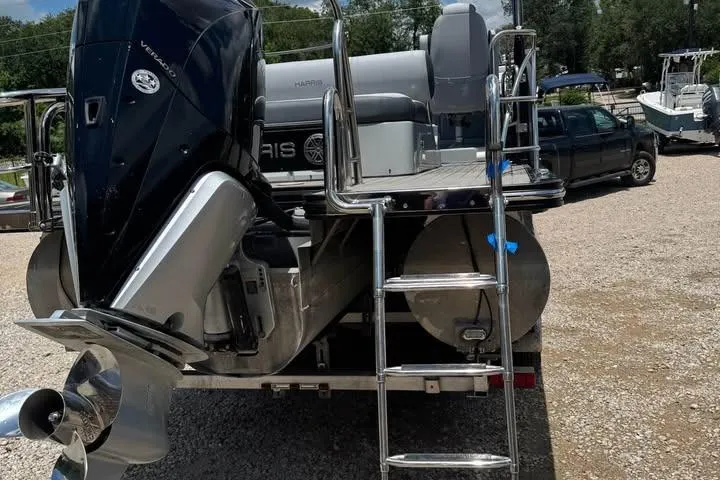 Slide: The Image of 2020 Harris Solstice 250 pontoon boat with powerful outboard motor and ladder, parked on gravel. - 5