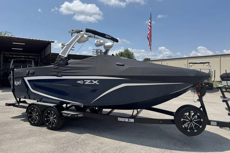 Slide: The Image of 2021 Tigé 23ZX boat on trailer, covered, with American flag in background. - 16