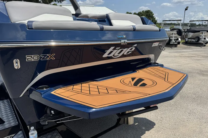 Slide: The Image of 2021 Tigé 23ZX boat rear view with swim platform, blue and tan design. - 2