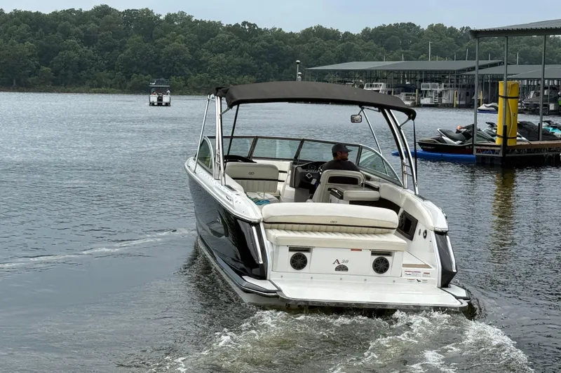 Slide: The Image of 2013 Cobalt A28 boat cruising on a lake near a marina with lush green trees. - 11