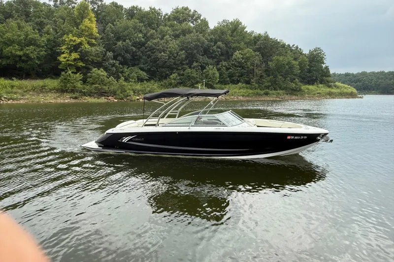 Slide: The Image of 2013 Cobalt A28 boat cruising on a serene lake with lush green forest backdrop. - 12