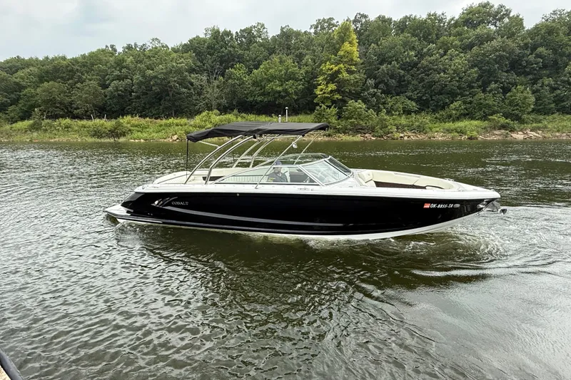 Slide: The Image of 2013 Cobalt A28 boat cruising on a calm river with lush green forest backdrop. - 2