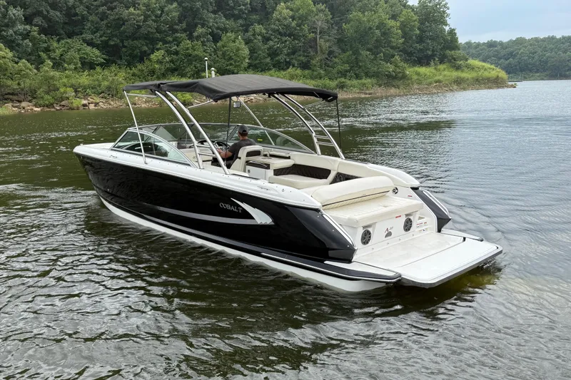 Slide: The Image of 2013 Cobalt A28 boat cruising on a serene lake with lush green shoreline. - 5
