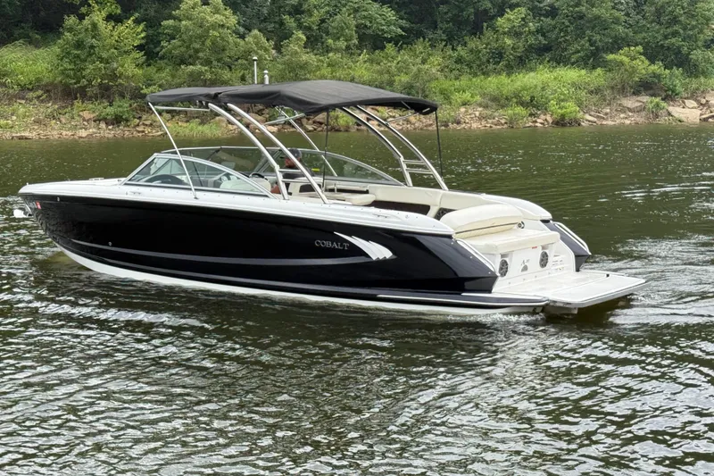 Slide: The Image of 2013 Cobalt A28 boat cruising on a calm lake with lush green shoreline. - 6