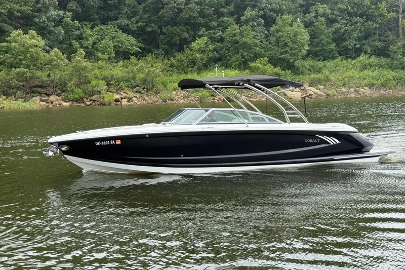 Slide: The Image of 2013 Cobalt A28 boat cruising on a calm lake with lush green forest backdrop. - 9