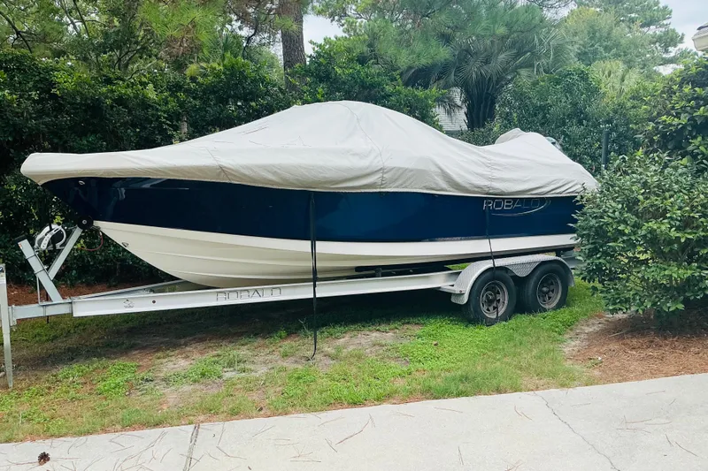 Slide: The Image of 2019 Robalo R207 Dual Console boat covered on trailer, surrounded by greenery. - 10