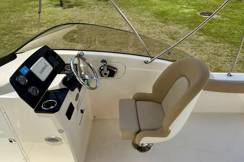 Slide: The Image of 2023 Scout 215 Dorado boat cockpit with steering wheel and beige captain's chair. - 13
