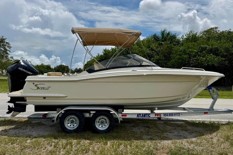 Slide: The Image of 2023 Scout 215 Dorado boat on trailer, featuring a Mercury engine and beige canopy. - 2