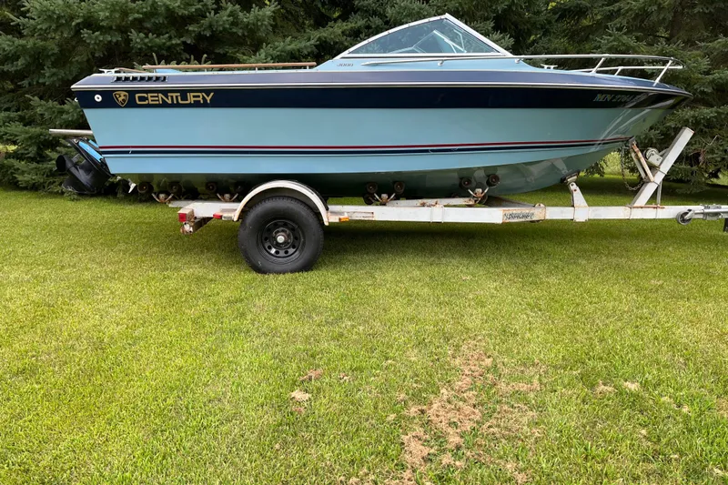 Slide: The Image of 1983 Century 3000 Bowrider boat on trailer, parked on grass with trees in background. - 2