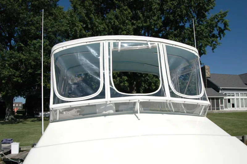 Slide: The Image of 1987 Bertram 33 Sport Fisherman boat with clear enclosure, docked near trees and buildings. - 24