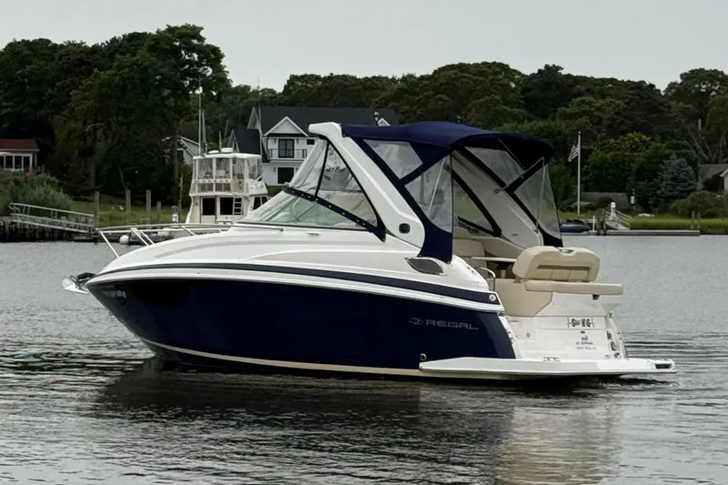 Slide: The Image of 2020 Regal 28 Express boat on calm water, surrounded by lush greenery and houses. - 5