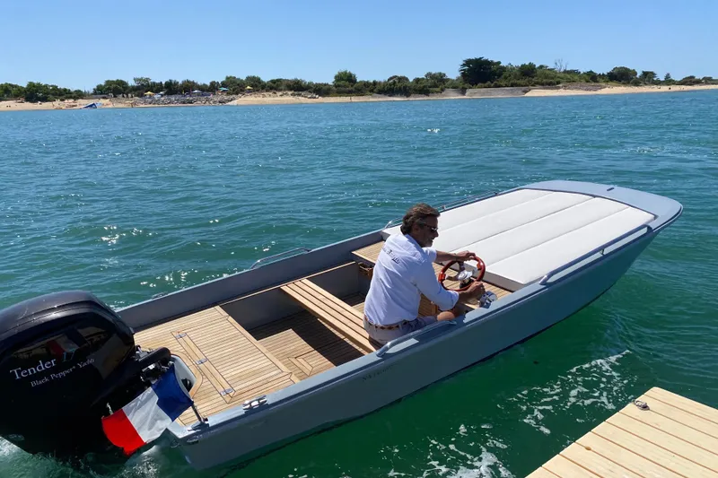Slide: The Image of Man steering Black Pepper Tender 17 boat on clear blue water, near a sunny shoreline. - 11