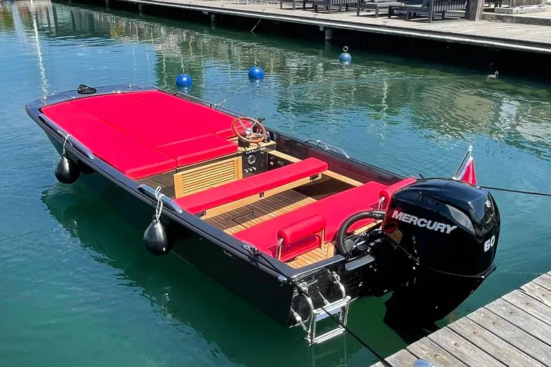 The Image of 2026 Black Pepper Tender 17 boat with red seating, docked on calm water. - 1