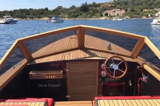 Slide: The Image of 2026 Black Pepper Tender 24 boat with wooden deck, steering wheel, and scenic coastal view. - 4