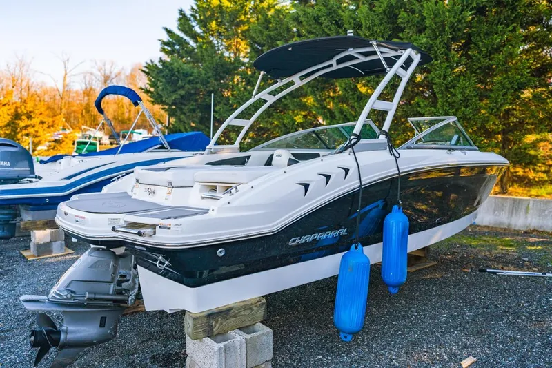 Slide: The Image of 2018 Chaparral 210 Suncoast boat on display with blue fenders, parked outdoors. - 3
