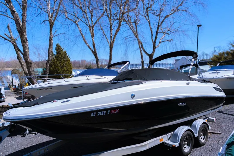 Slide: The Image of 2012 Sea Ray 240 Sundeck boat on trailer, parked outdoors near trees. - 0