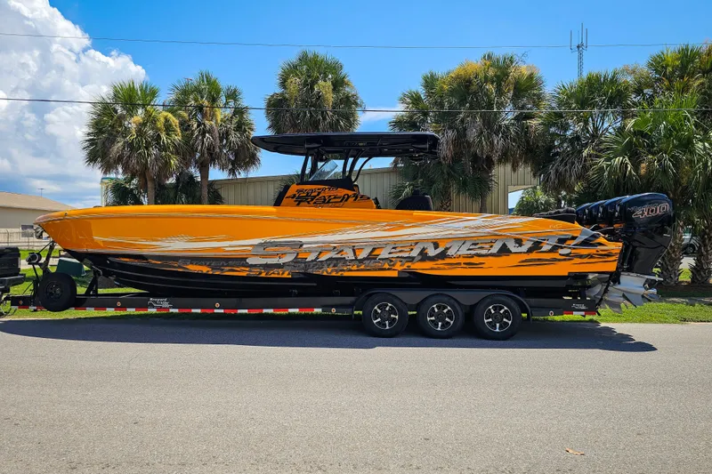 The Image of 2016 Statement 380 Open boat on trailer, vibrant orange design, parked near palm trees. - 1