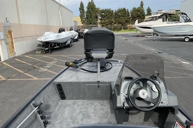Slide: The Image of 2026 Tracker Bass Tracker Classic XL boat interior with steering wheel and motor, parked outdoors. - 16