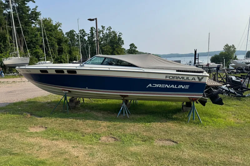 The Image of 1984 Formula 272 Adrenaline boat on stands, surrounded by greenery and other boats. - 1