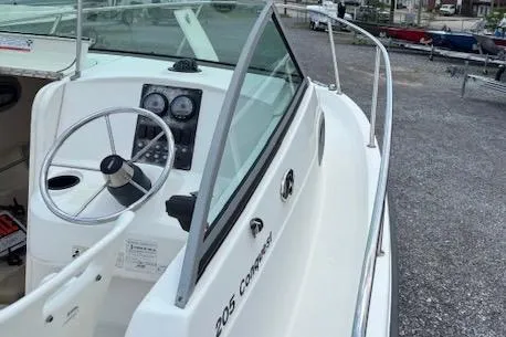 Slide: The Image of 2006 Boston Whaler 205 Conquest boat with steering wheel and dashboard, docked on gravel. - 7