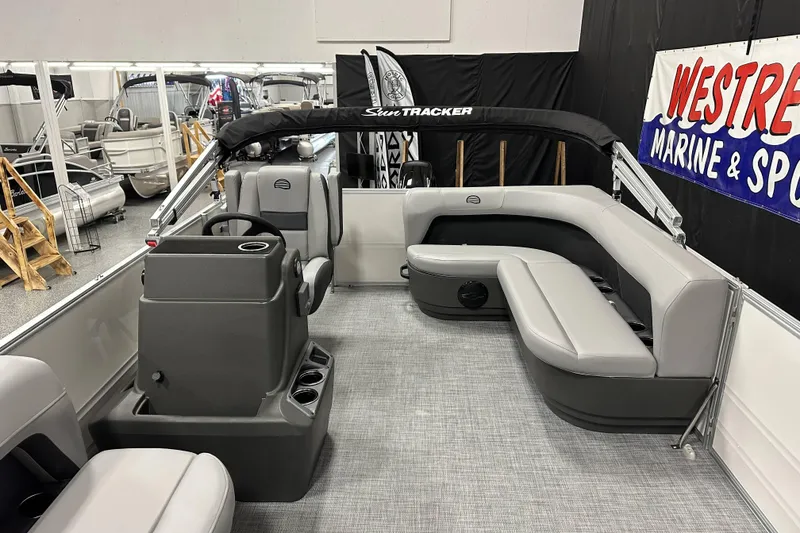Slide: The Image of 2026 Sun Tracker Party Barge 16 DLX interior with seating and steering console in showroom. - 18