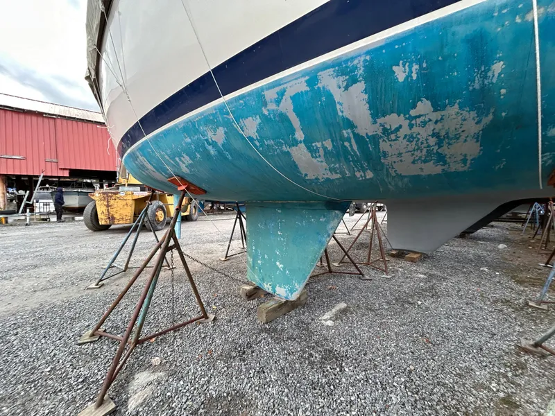 Slide: The Image of 1985 Pearson P-28 sailboat on stands, showing weathered blue hull in a boatyard. - 5