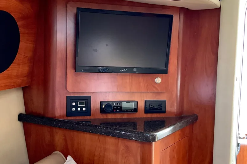 Slide: The Image of 2013 Rinker 290 Express Cruiser interior with TV and control panel on wood finish. - 17