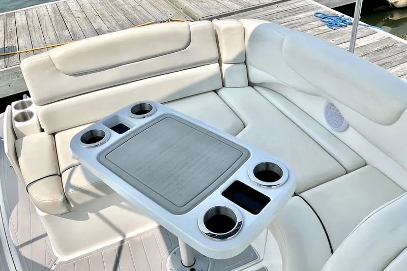 Slide: The Image of 2013 Rinker 290 Express Cruiser interior with cushioned seating and table, docked at marina. - 6