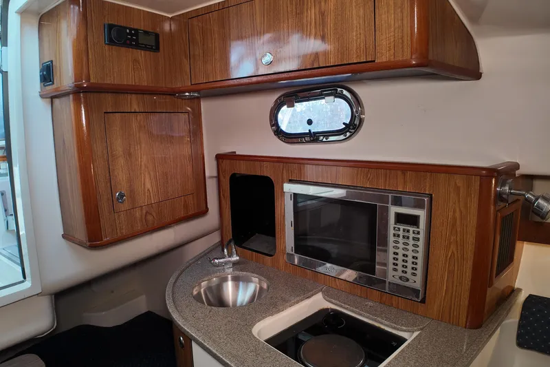 Slide: The Image of 2007 Pursuit 285 Offshore boat interior with wood cabinetry, microwave, sink, and porthole window. - 30