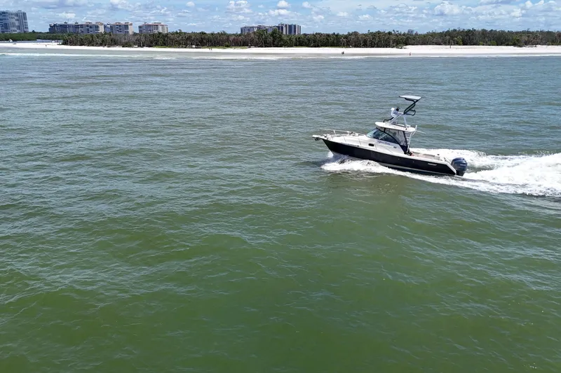 Slide: The Image of 2007 Pursuit OS 285 Offshore boat cruising near a sandy shoreline under a clear blue sky. - 36