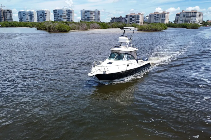 Slide: The Image of 2007 Pursuit OS 285 Offshore boat cruising near coastal buildings and greenery. - 5