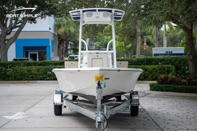 Slide: The Image of 2024 Sea Pro 208 Bay boat on trailer, parked outdoors with trees and building in background. - 5