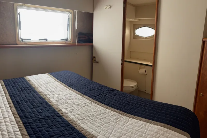 Slide: The Image of 1999 Silverton 392 yacht bedroom with ensuite bathroom, featuring a striped bedspread and window. - 15