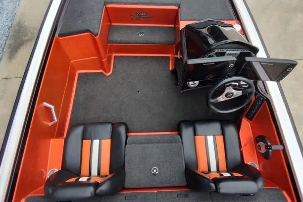 Slide: The Image of 2016 Bullet 21XRD boat interior with orange and black seating, steering console, and carpeted flooring. - 9