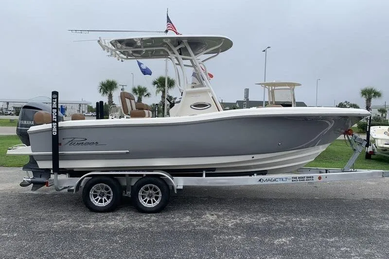 Slide: The Image of 2025 Pionee Sportfish 222 boat on trailer, parked outdoors with flags and palm trees. - 5
