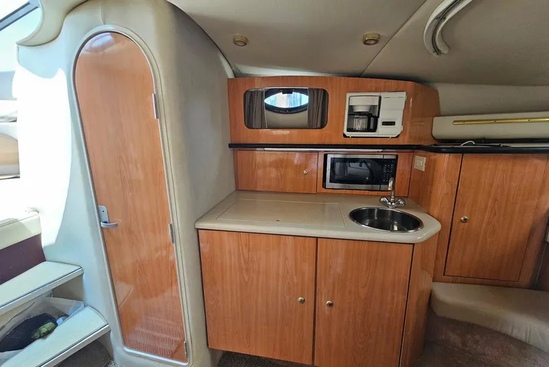 Slide: The Image of 1999 Regal Commodore 292 boat interior with kitchenette, featuring wood cabinets, sink, microwave, and coffee maker. - 20