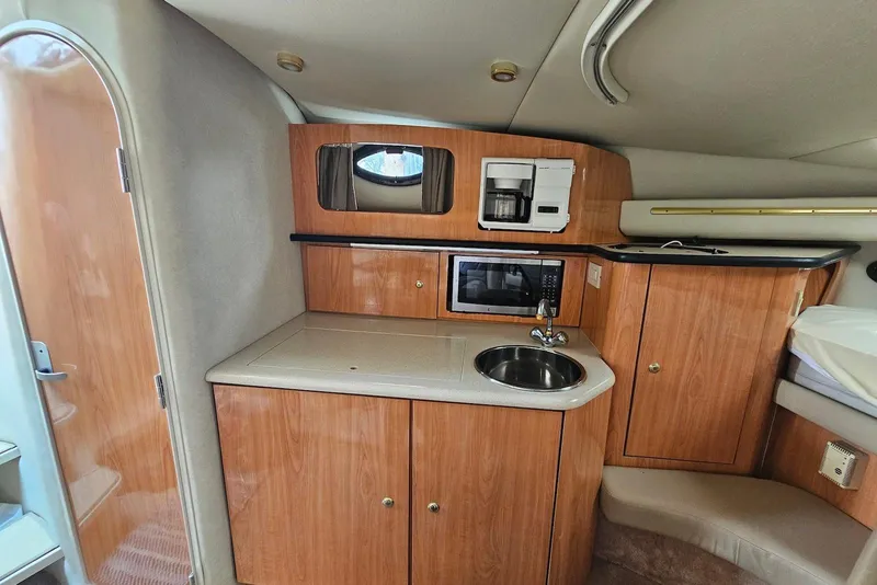 Slide: The Image of 1999 Regal Commodore 292 boat interior with kitchenette, featuring wood cabinets, sink, microwave, and coffee maker. - 21