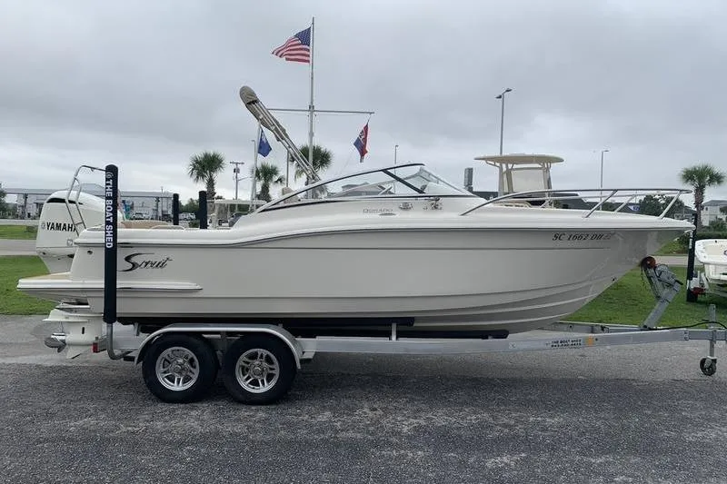 Slide: The Image of 2018 Scout 225 Dorado boat on trailer, parked outdoors with flags in background. - 5
