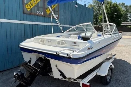 Slide: The Image of 2006 Bayliner 185 Bowrider boat on trailer, blue and white, parked near blue building. - 3