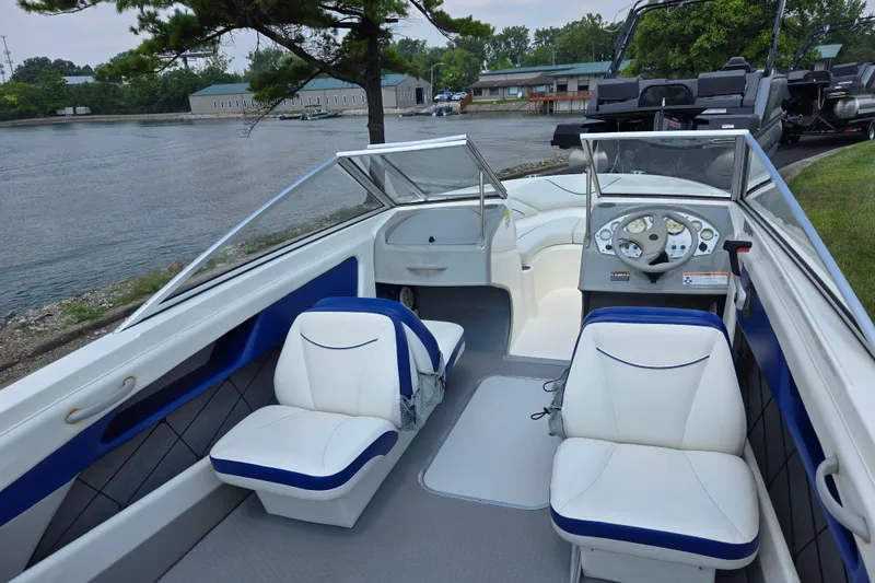 Slide: The Image of 2006 Bayliner 195 Classic boat interior with white and blue seating, docked by a lake. - 10