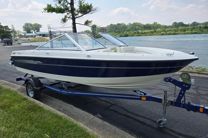 Slide: The Image of 2006 Bayliner 195 Classic boat on trailer by a riverside, under a partly cloudy sky. - 8