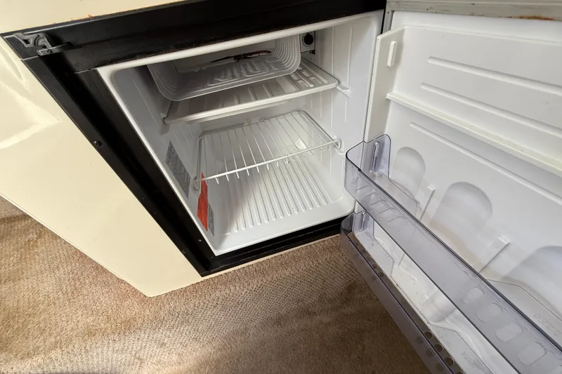 Slide: The Image of Open mini fridge inside 2000 Rinker 270 Fiesta Vee boat, showing empty shelves. - 27