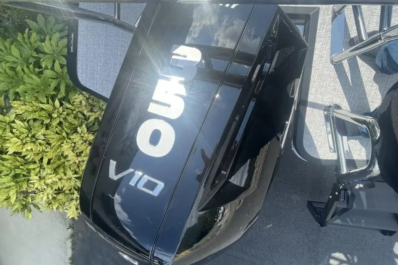 Slide: The Image of 2026 Harris Grand Mariner 250 boat engine, V10, with reflective black surface and nearby greenery. - 3