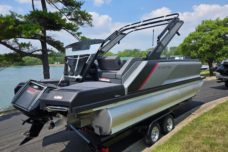 Slide: The Image of 2024 Manitou Explore pontoon boat with sleek design, parked by a scenic lake. - 1