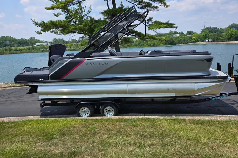 Slide: The Image of 2024 Manitou Explore pontoon boat on trailer by a scenic lake. - 10