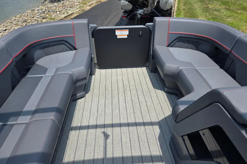 Slide: The Image of 2024 Manitou Explore boat interior with gray seating and red accents, dockside view. - 20