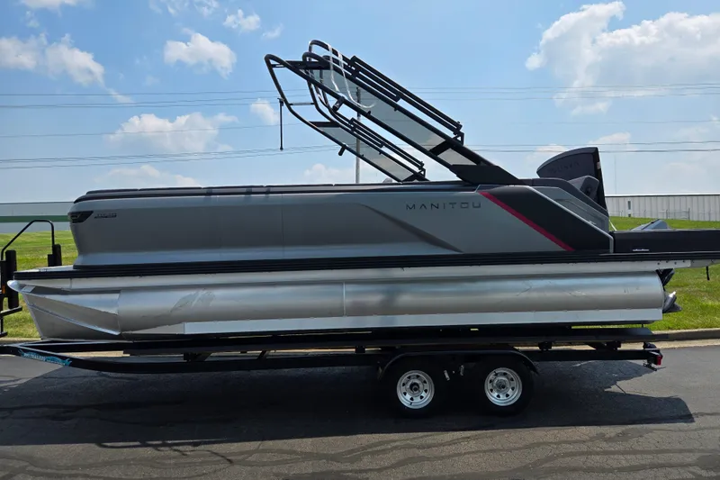 Slide: The Image of 2024 Manitou Explore pontoon boat on trailer under blue sky. - 4