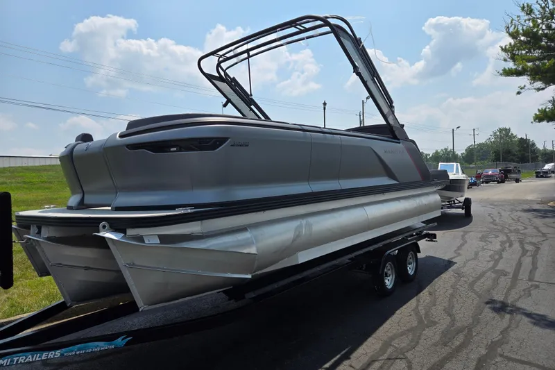 Slide: The Image of 2024 Manitou Explore pontoon boat on trailer, parked outdoors under a cloudy sky. - 5