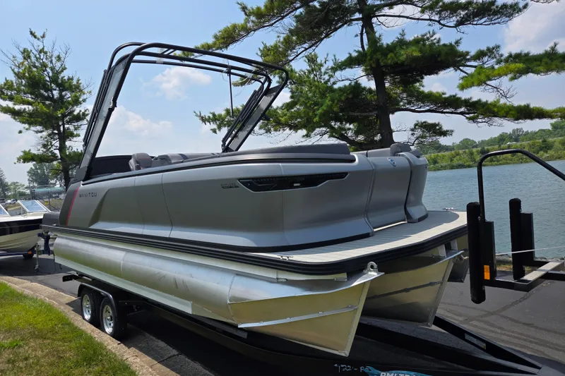 Slide: The Image of 2024 Manitou Explore pontoon boat on trailer by a lake, under clear sky. - 9