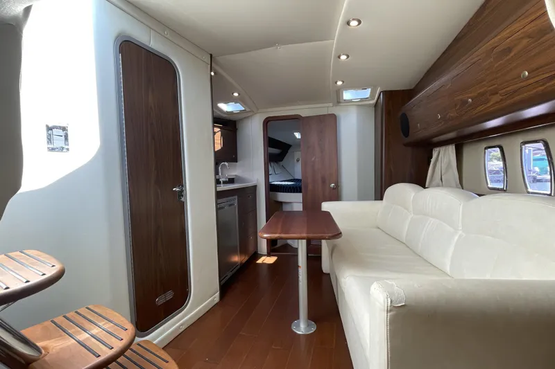 Slide: The Image of 2017 Rinker EX 370 yacht interior with white sofa, wooden table, and cabin windows. - 24